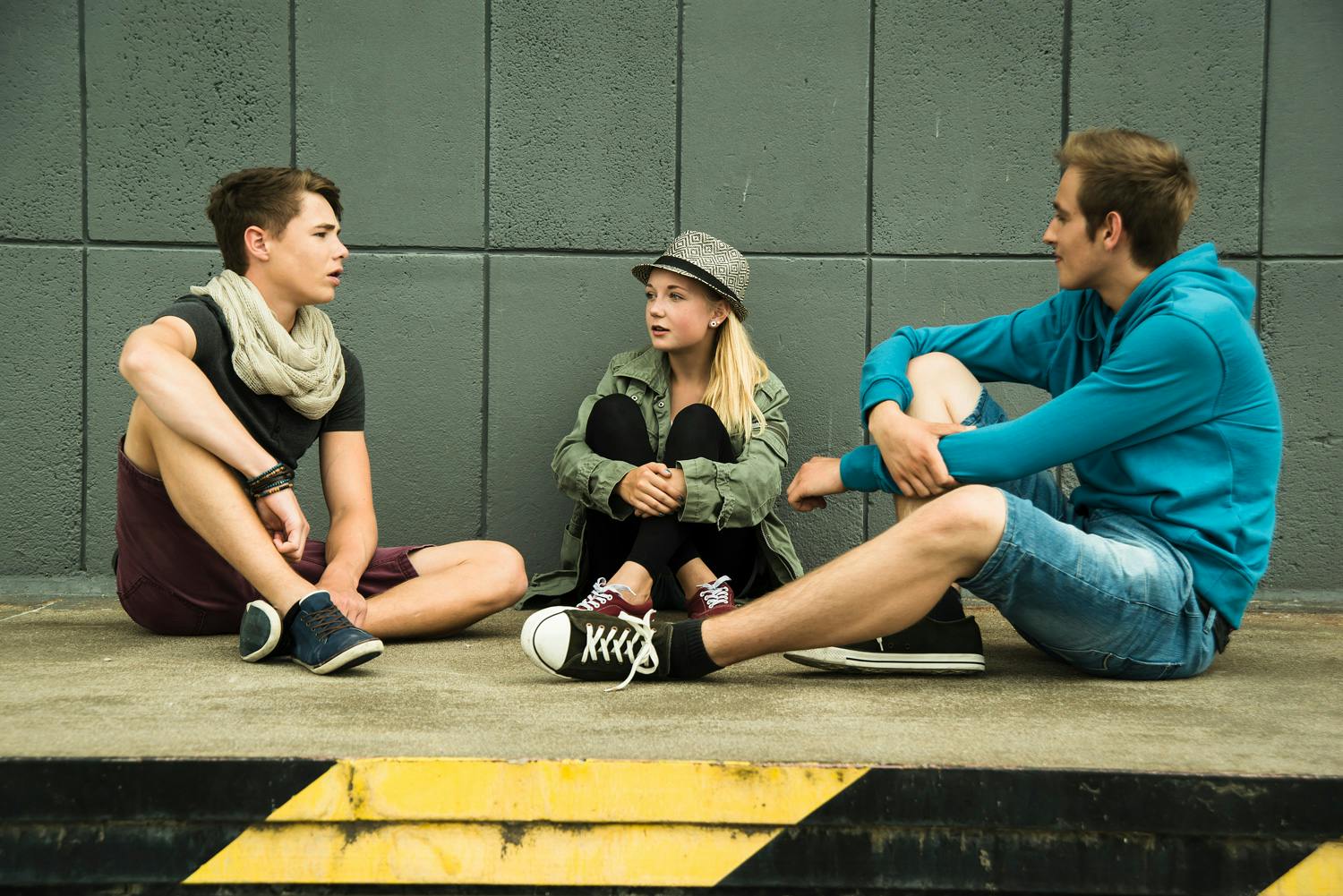 Two boys and a girl sitting on the sidewalk